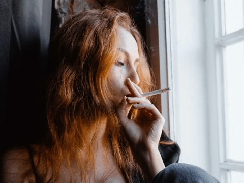 Red haired girl smoking near window
